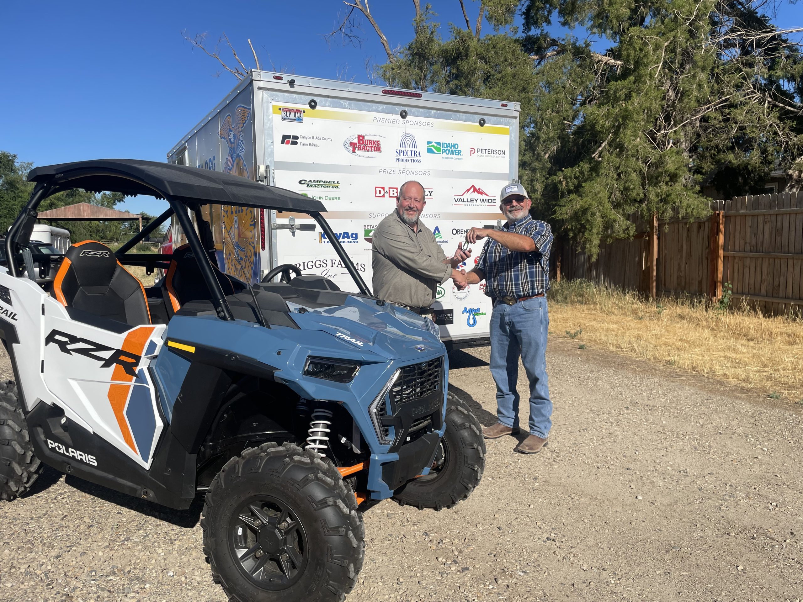 Two people shaking hands next to a UTV and trailer