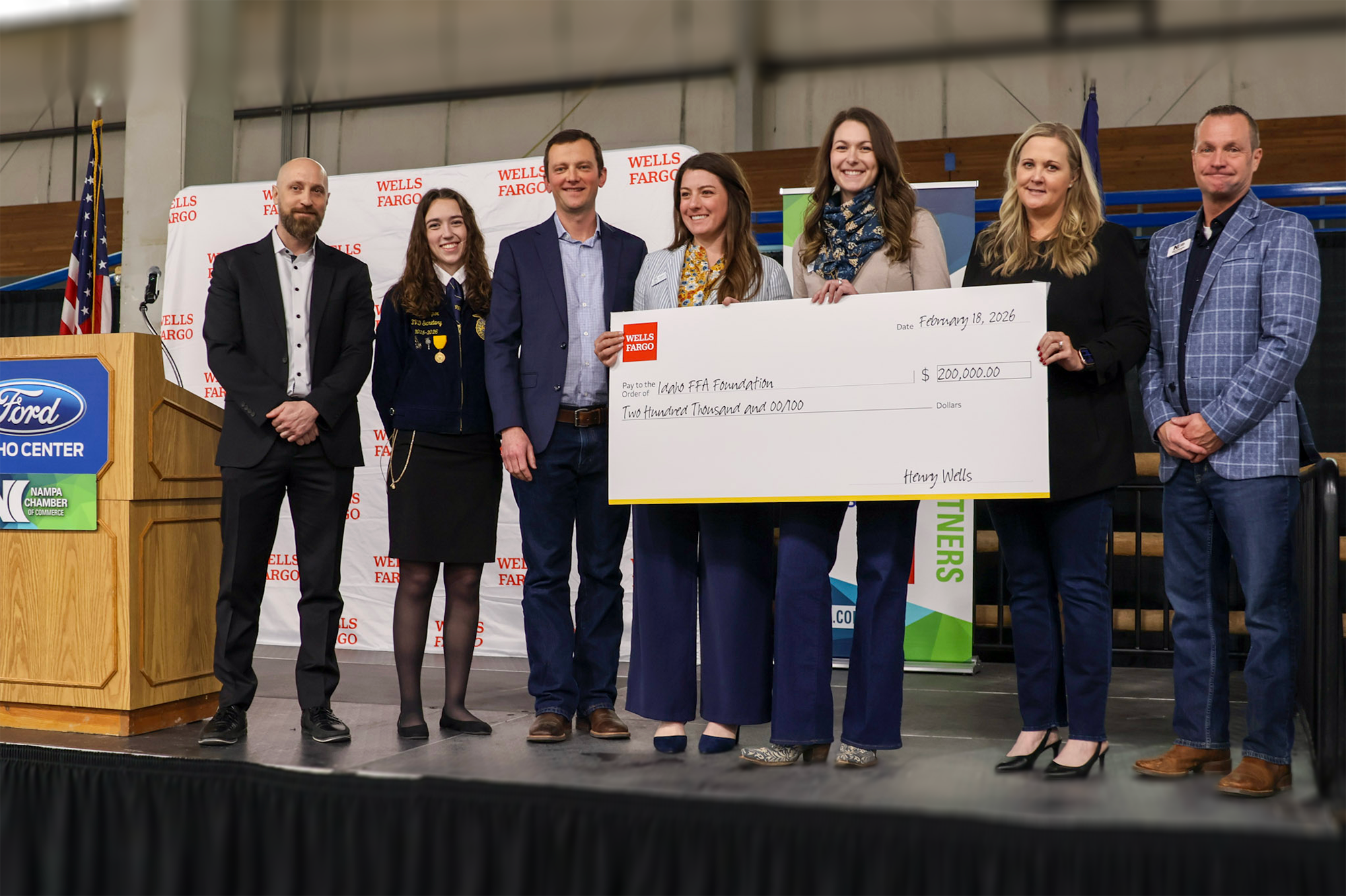 Seven people smiling on stage with a donation check